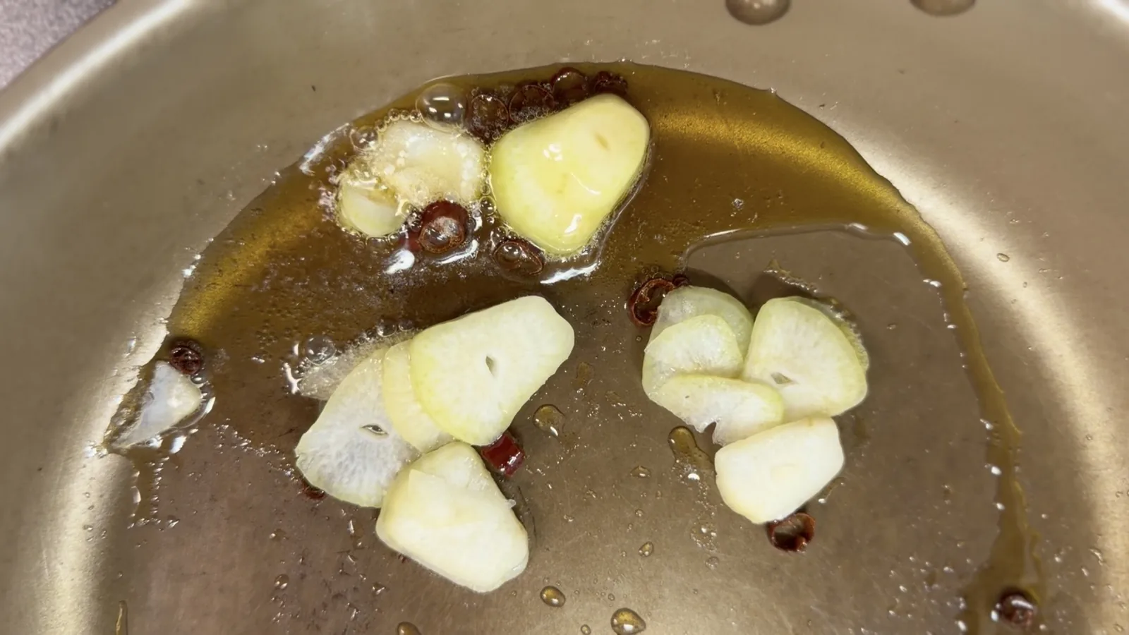 ごま油の中でにんにくの薄切りと輪切り唐辛子を熱しているフライパン