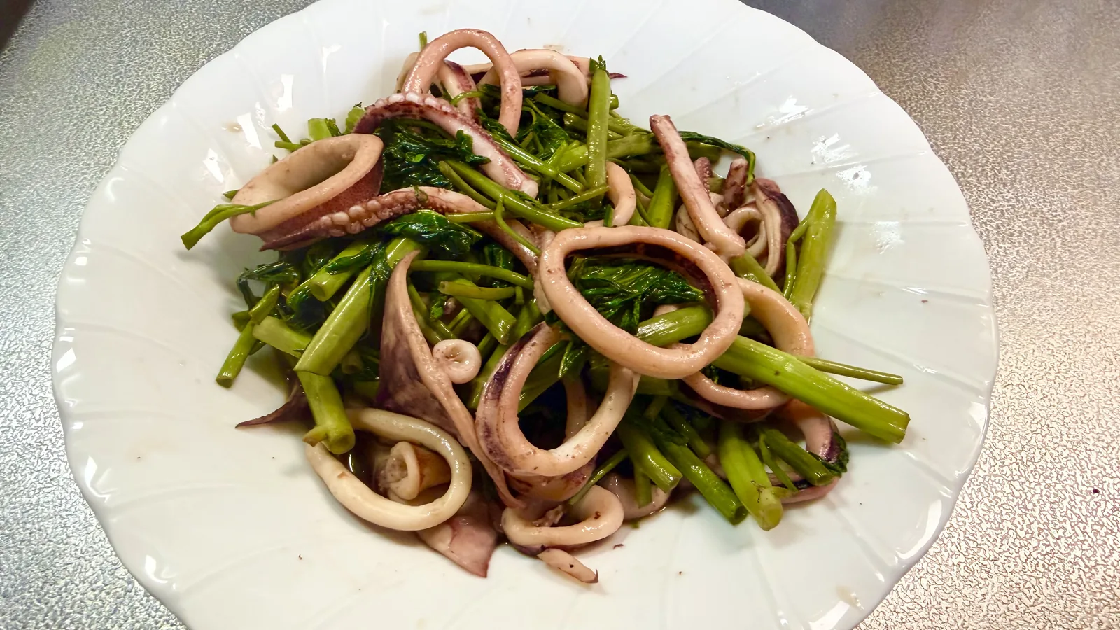 白い皿に盛りつけたいかと空芯菜の炒め物